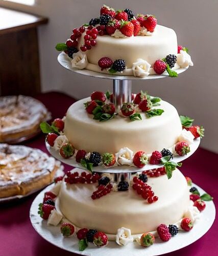 Gateau de mariage deposé sur une table avec une decoration des fleurs rouge et vert