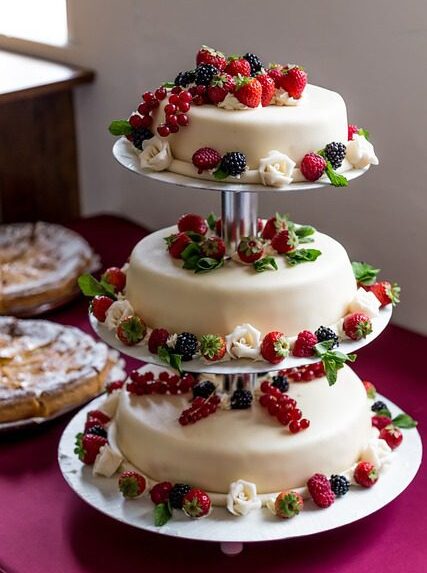 Gateau de mariage deposé sur une table avec une decoration des fleurs rouge et vert